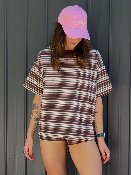 Person wearing a striped shirt, pink cap, and gray slippers standing against a metallic wall.