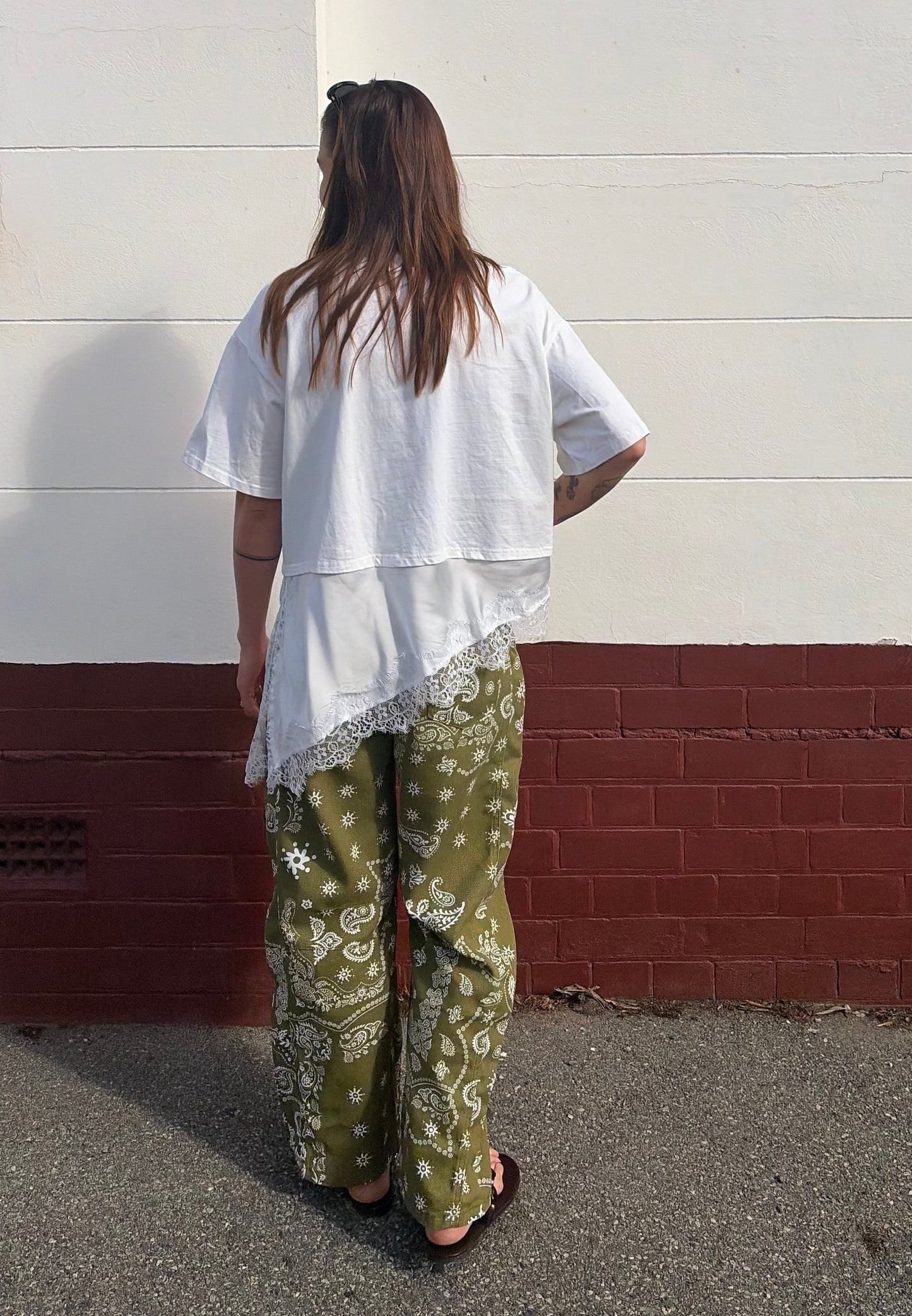 Person wearing a white top and green patterned pants standing against a white wall with a red base.