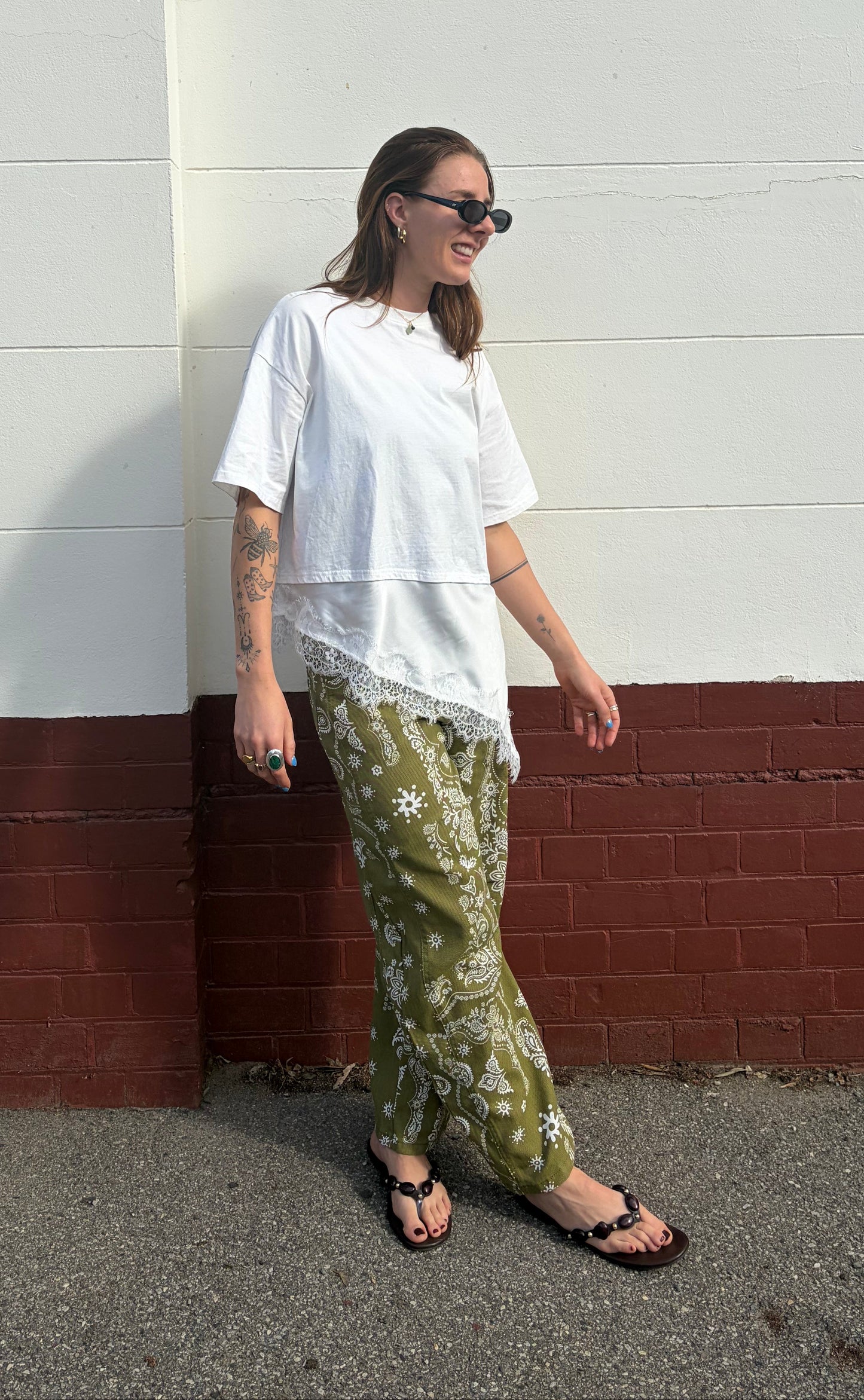 Person wearing a white shirt and green camouflage pants standing on a street corner.
