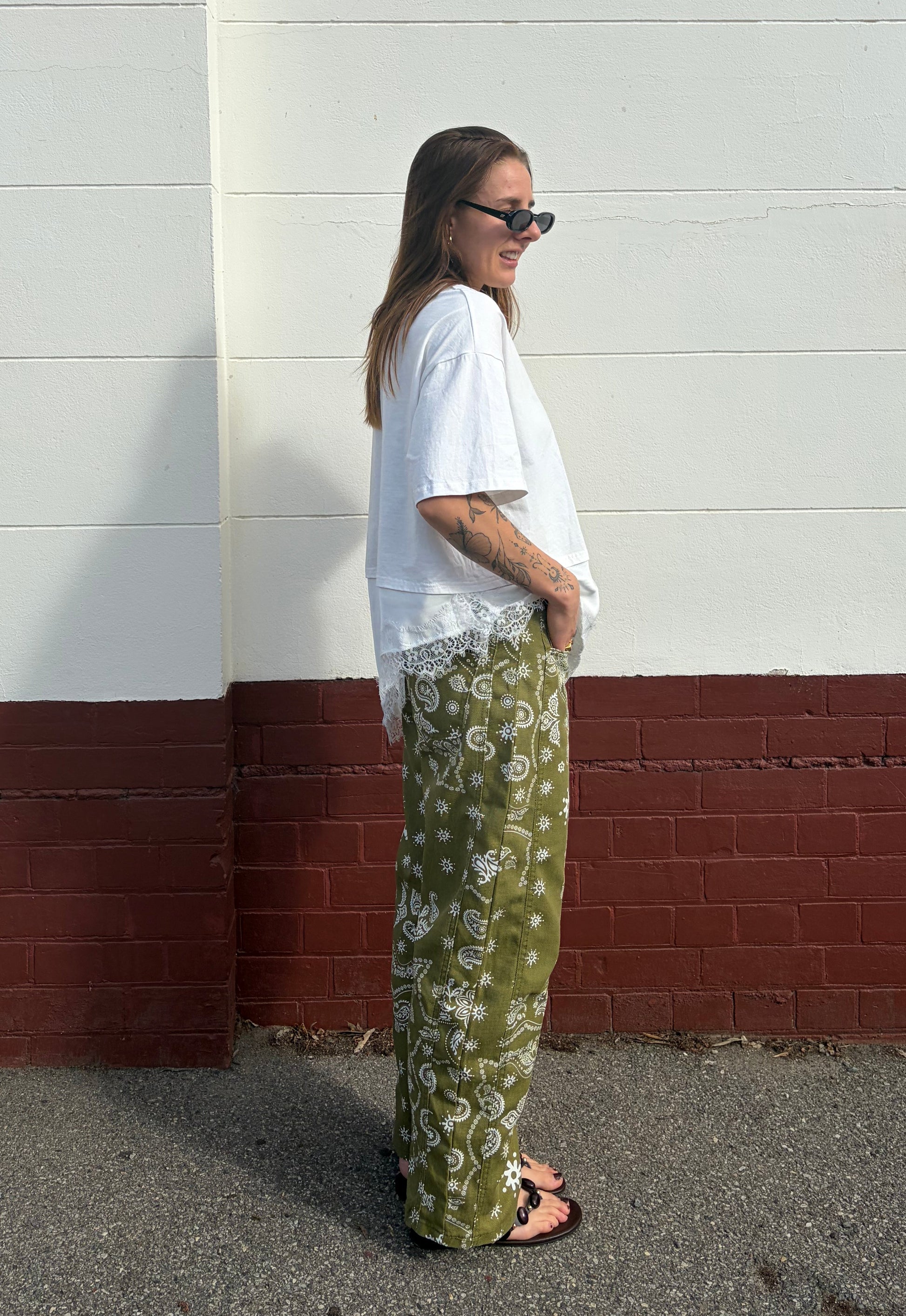 Person wearing a white shirt and green patterned pants standing against a white wall with a red base.
