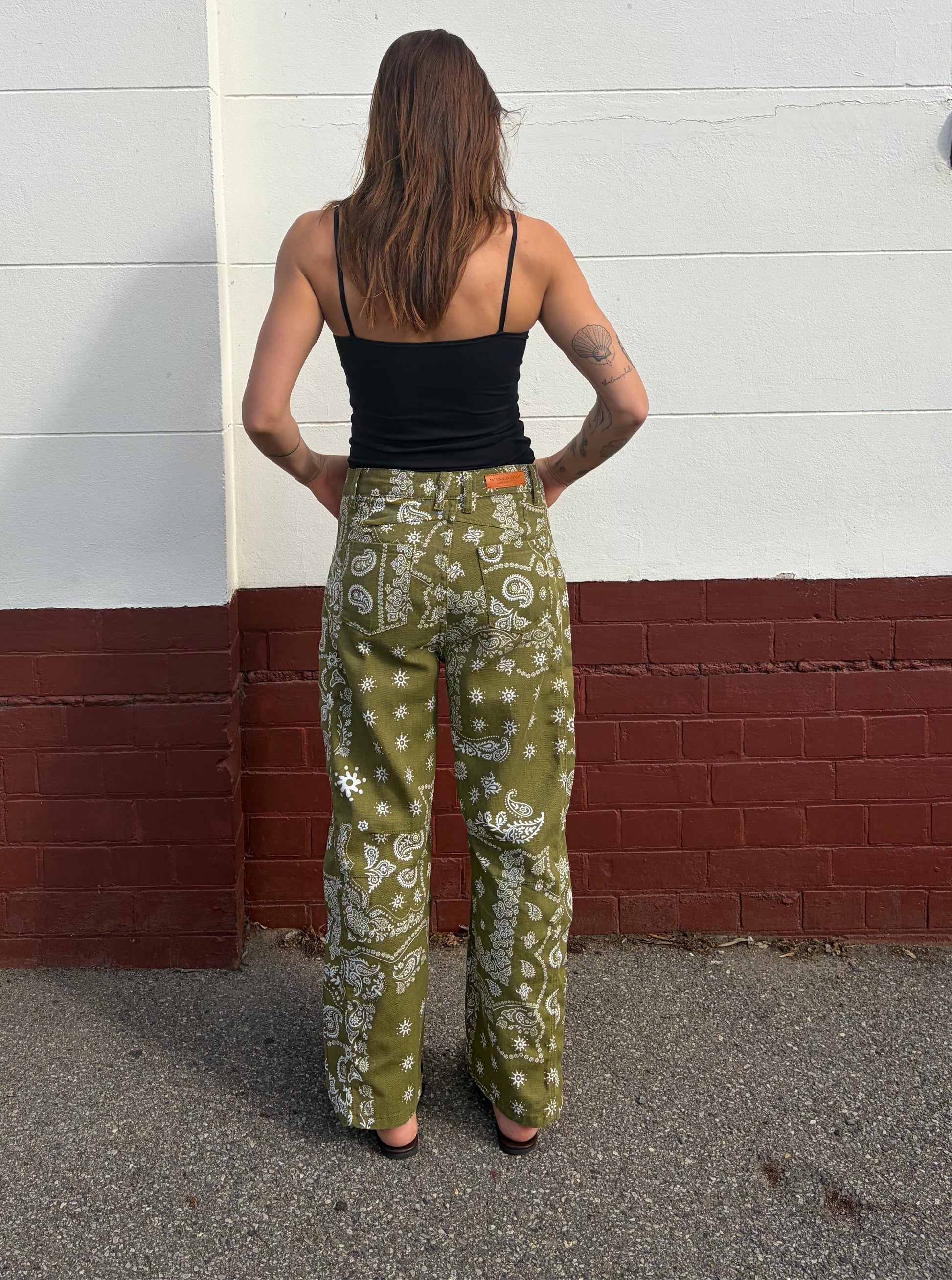 Person wearing a black top and green floral pants standing on a street corner.