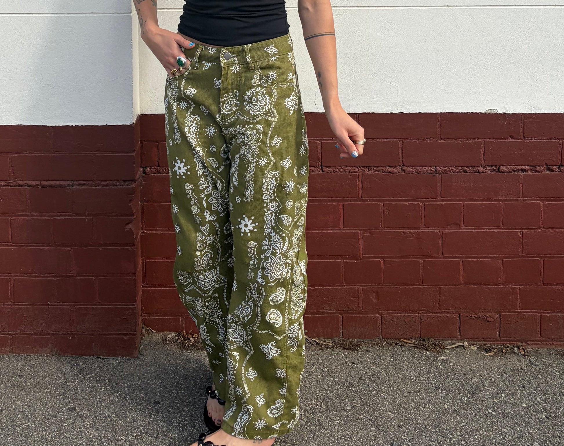 Person wearing a black top and green patterned pants standing on a reflective surface.