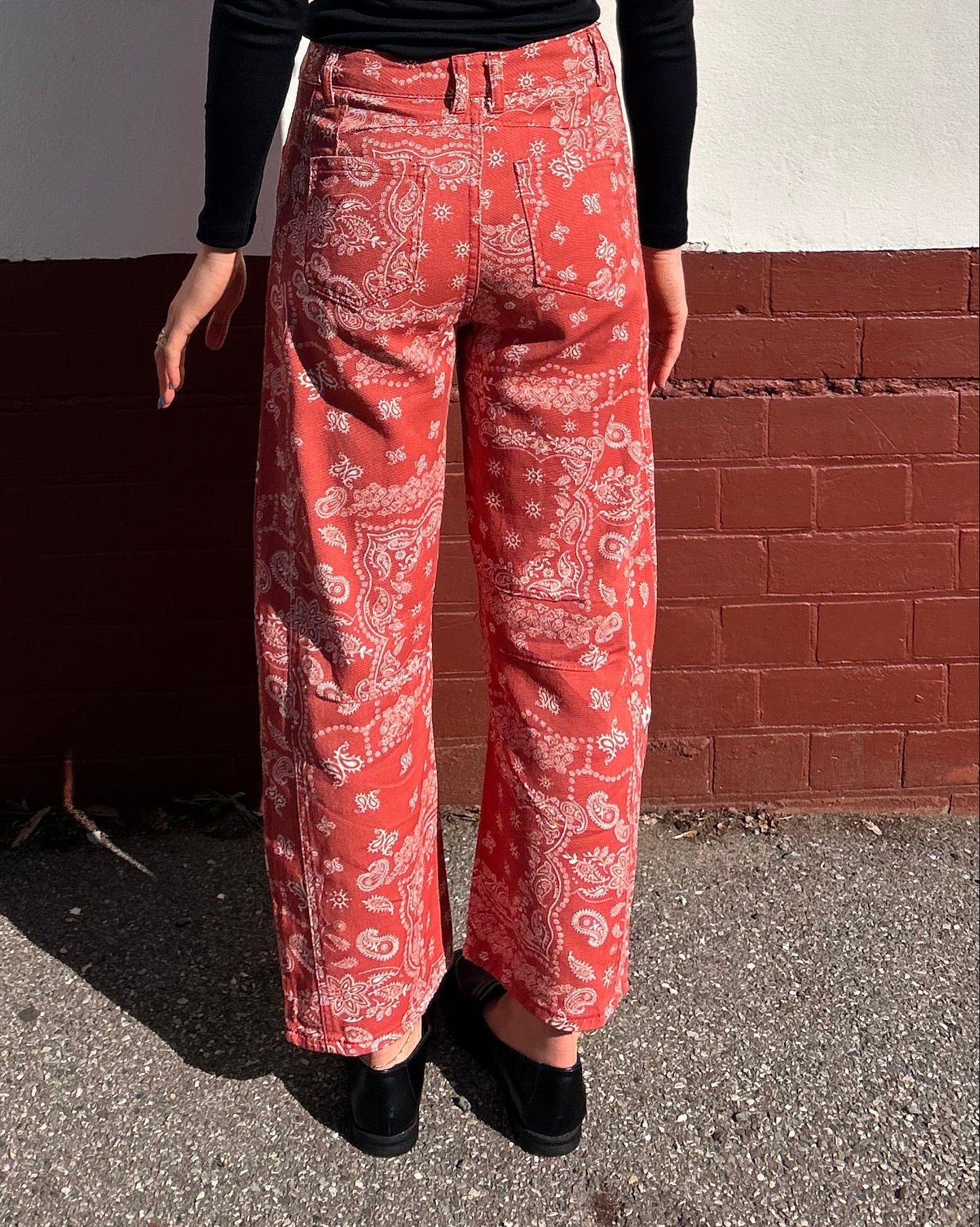 Person wearing a black top and red patterned pants standing on a street corner.